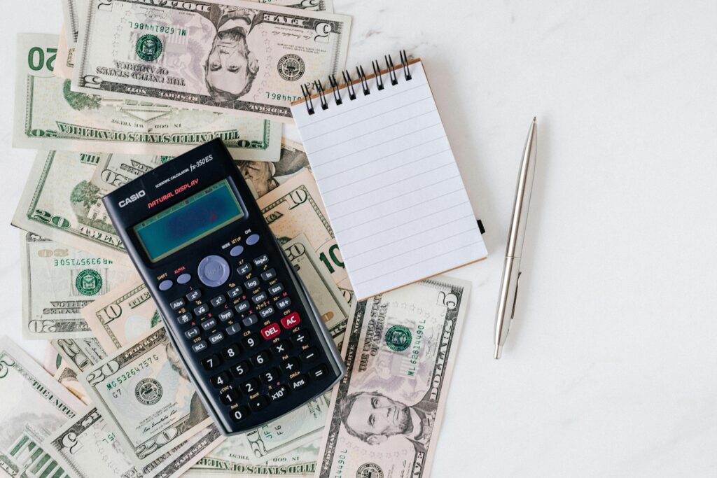 pexels-photo-4386373-4386373 Calculator and Notepad placed over Stack of Paper Bills